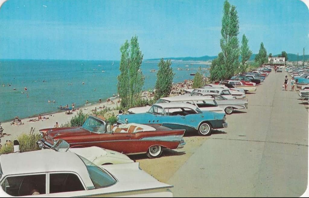 Vintage color postcard of finned cars parked beside Oval Beach