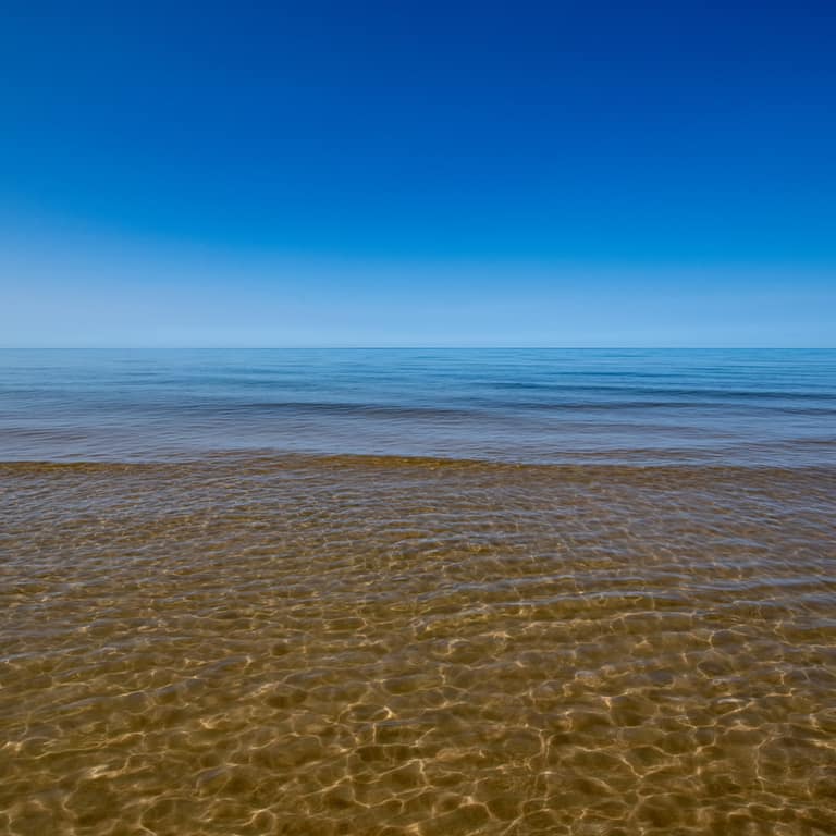 Calm, clear Lake Michigan water at Oval Beach under a blue sky